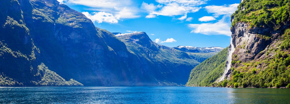 a blue fjord is greeted by mountains full of plant life