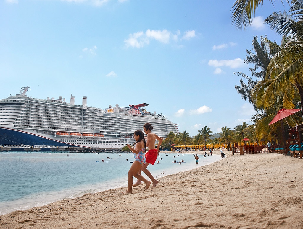 a carnival ship is docked at sea while kids play on the beach