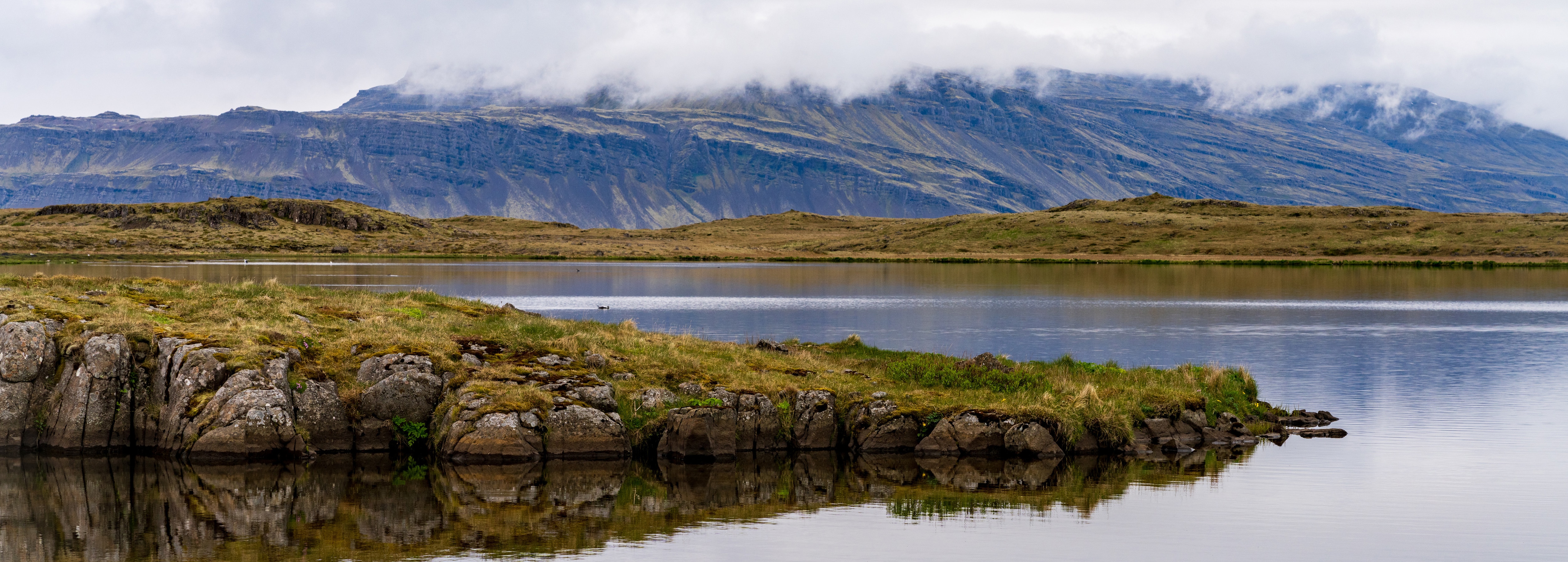 view of black sand beach and lagoon with mountains in the background in djupivogur