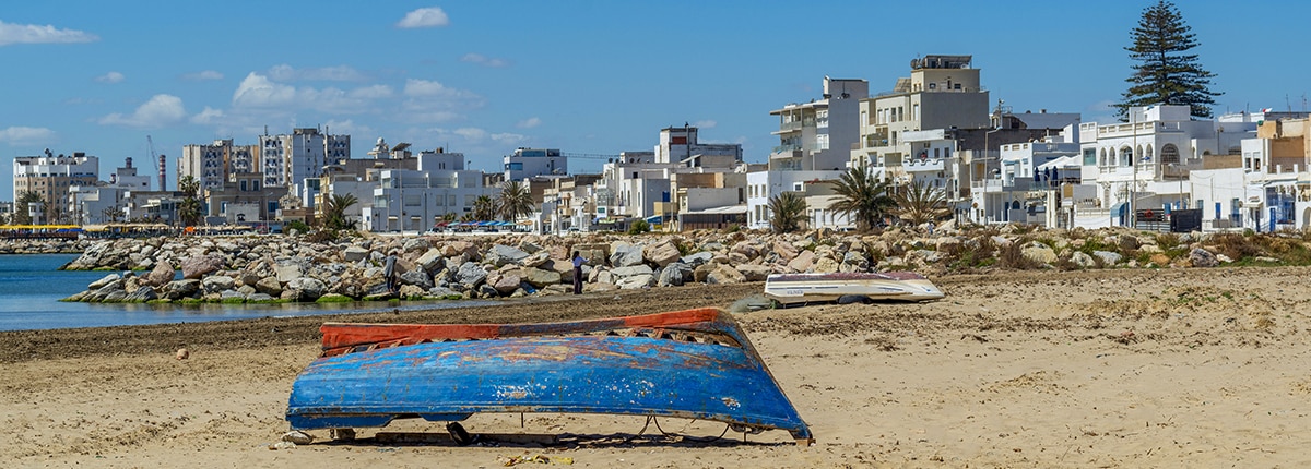 small blue boat on the shore of La Goulette with city in the background