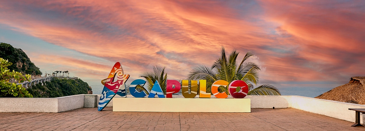 colorful acapulco sign with bright colorful letters with sunset and trees in the background