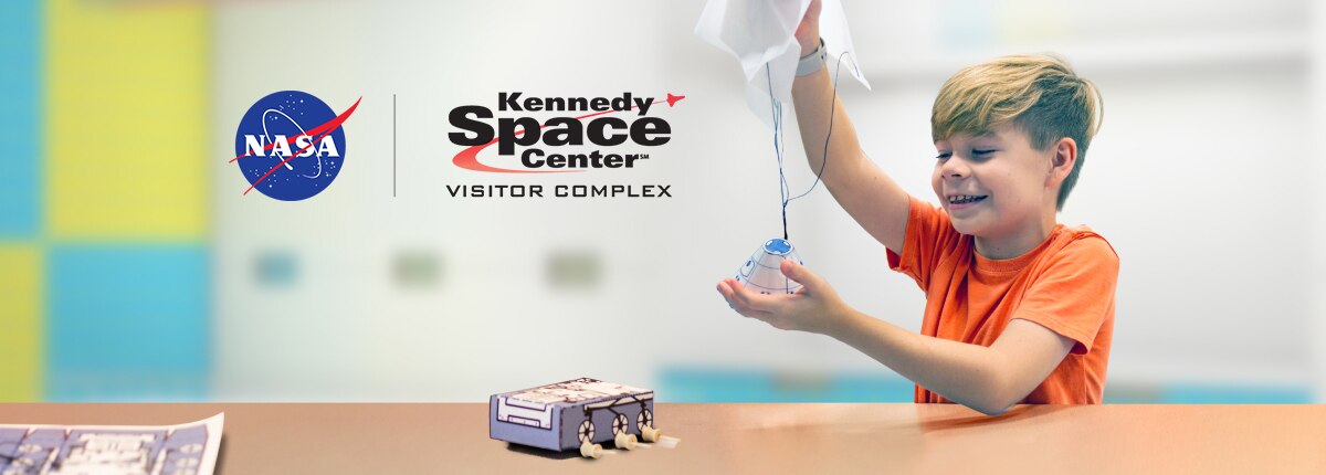 a boy plays with models of space rover and reentry capsule; nasa and kennedy space center logos
