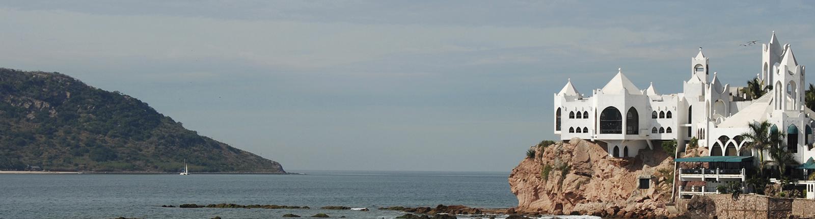 Beautiful white historic building surmounted upon a rock fixture with the ocean laying below