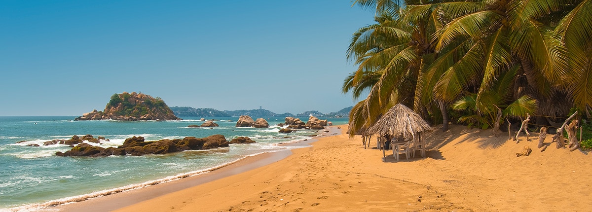 view of acapulco bay on a sunny day with beach cabanas and palm trees